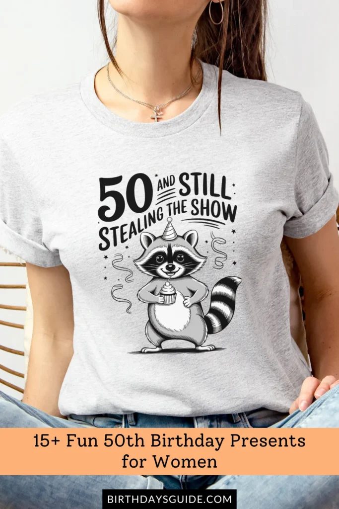  A heather gray birthday t-shirt featuring a cute raccoon wearing a party hat, holding a cupcake, with the phrase "50 and Still Stealing the Show.