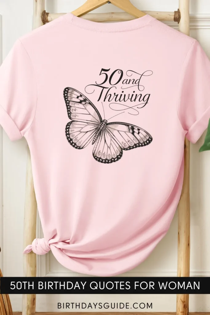 A pink birthday t-shirt with an elegant black-and-white butterfly illustration and the phrase "50 and Thriving" written in a cursive font.